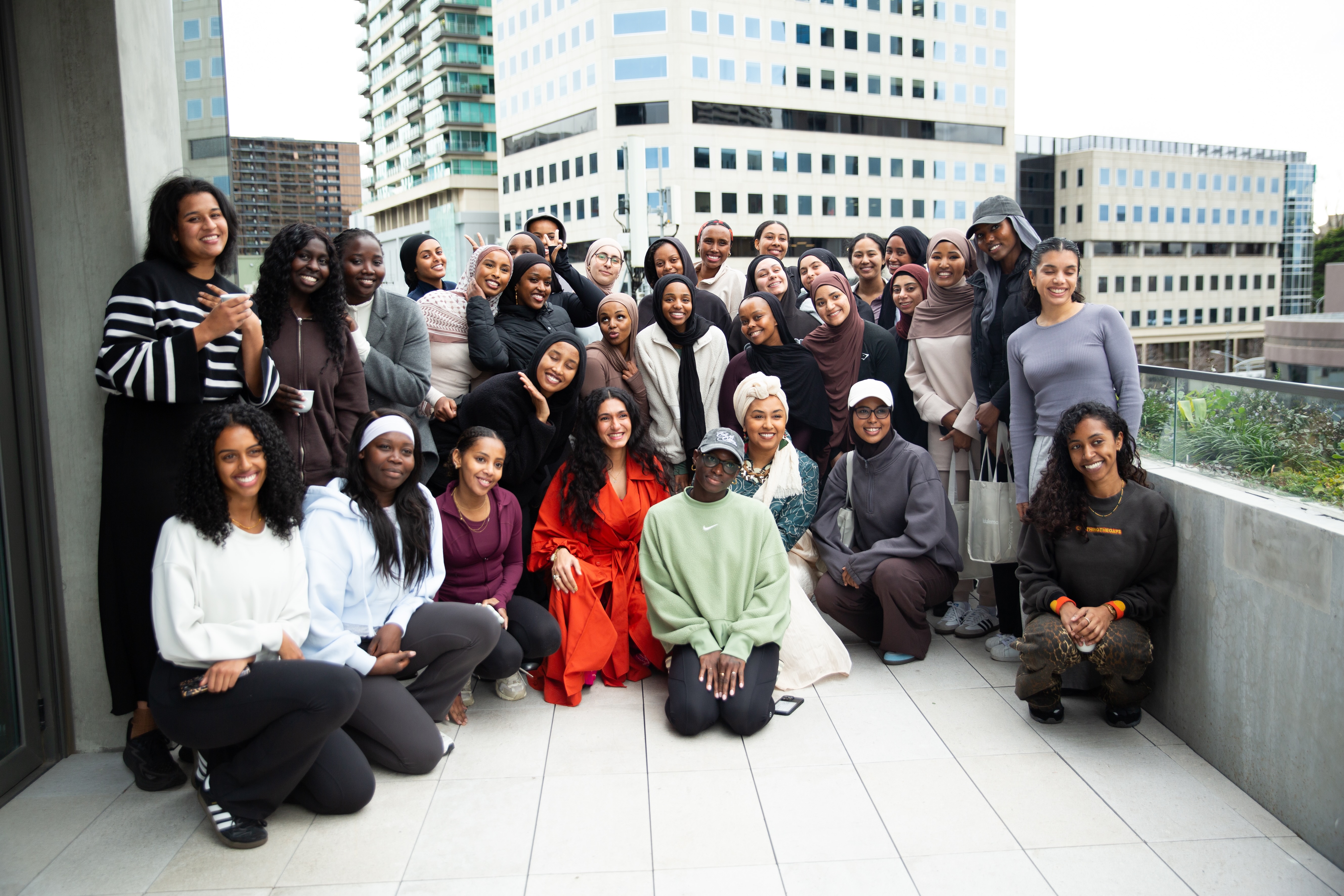 Group photo of women and girls gathered outdoors on a city terrace, smiling together after an event.